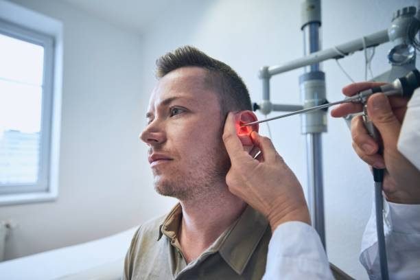 Patient at ENT clinic. Specialist doctor - Otolaryngologist doing ear examination of young man.